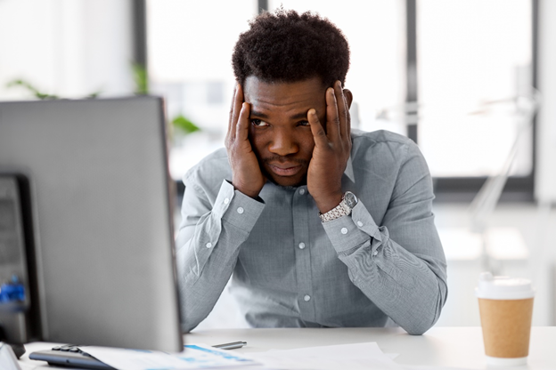 Man at computer holding his head.