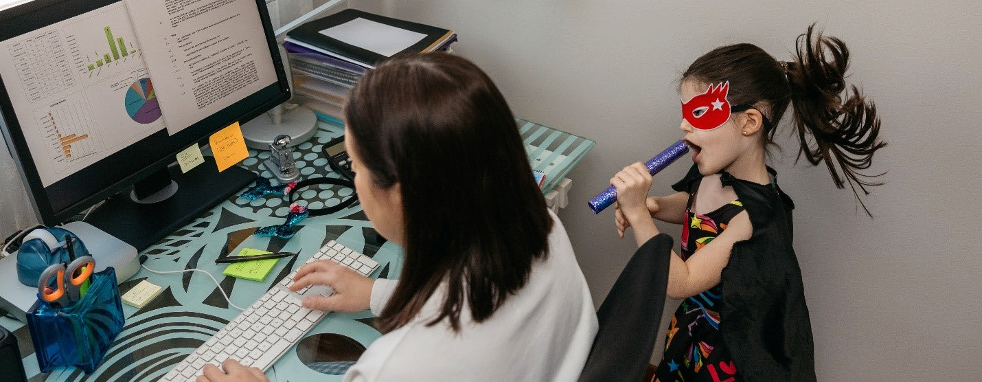 Mom working from home with child in costume next to her.