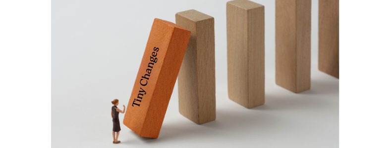 Woman pushing a domino labeled Tiny Changes which knocks over the next domono